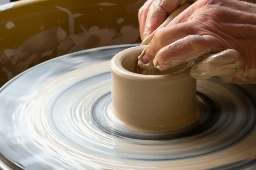 Hands shaping a cup on a pottery wheel